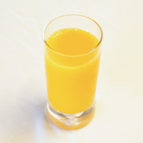 A tall glass filled with bright orange juice on a light background.