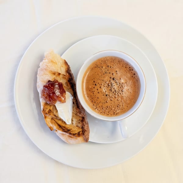 Overhead view of a foamy coffee and toast with jam and cream cheese on a white plate.