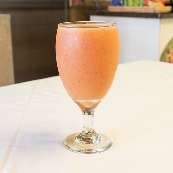 A frosty glass of orange-pink smoothie on a white tablecloth in a restaurant setting.
