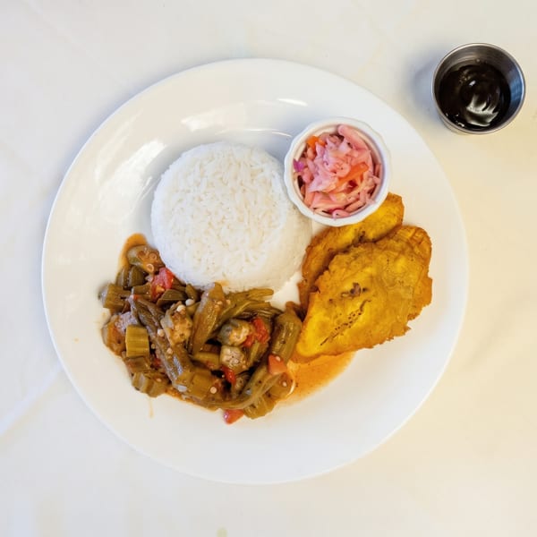 White plate with rice, okra stew, fried plantains, pickled vegetables, and a side of dark sauce.
