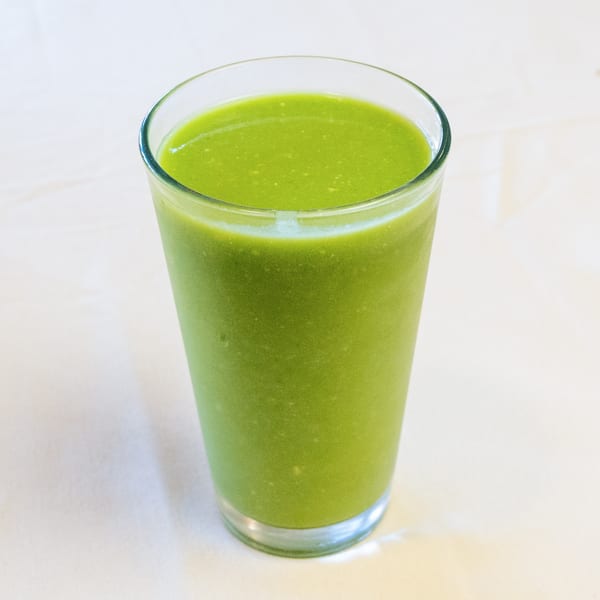 Vibrant green smoothie in a tall glass on a light-colored surface.
