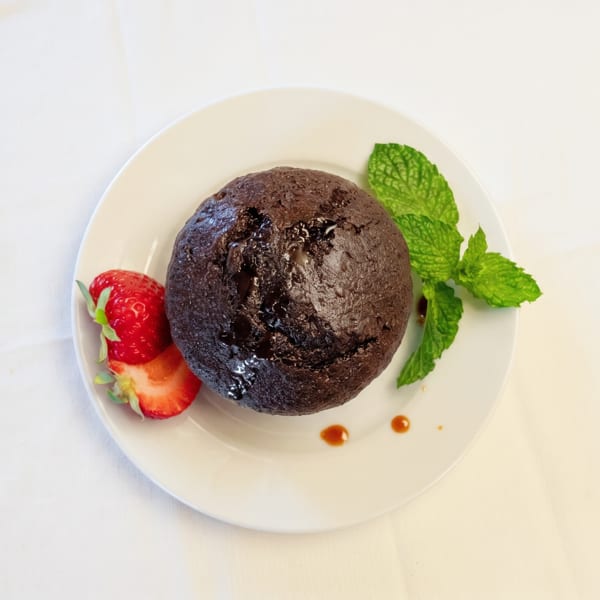 Chocolate lava cake with sliced strawberries and fresh mint on a white plate.