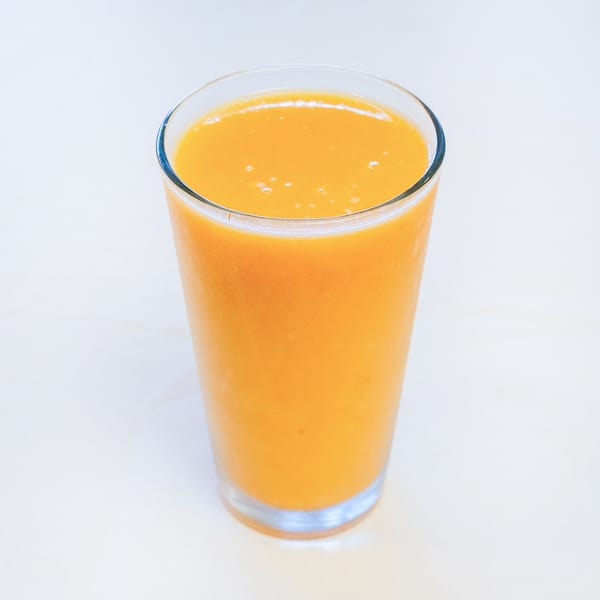 Tall glass of vibrant orange juice or smoothie on a light background.