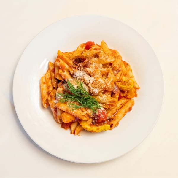 Penne pasta with red sauce, cherry tomatoes, yellow squash, and fresh dill on a white plate.