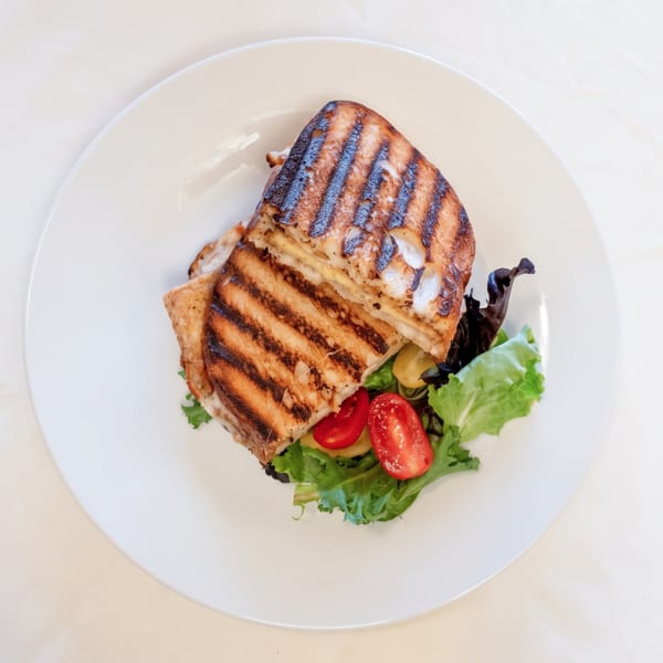 Golden grilled panini sandwich with a fresh side salad of lettuce and cherry tomatoes.