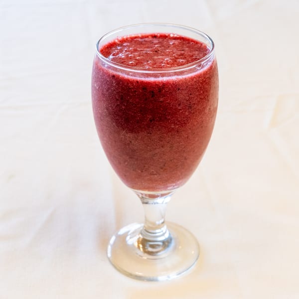 A red berry smoothie in a stemmed glass on a light table.
