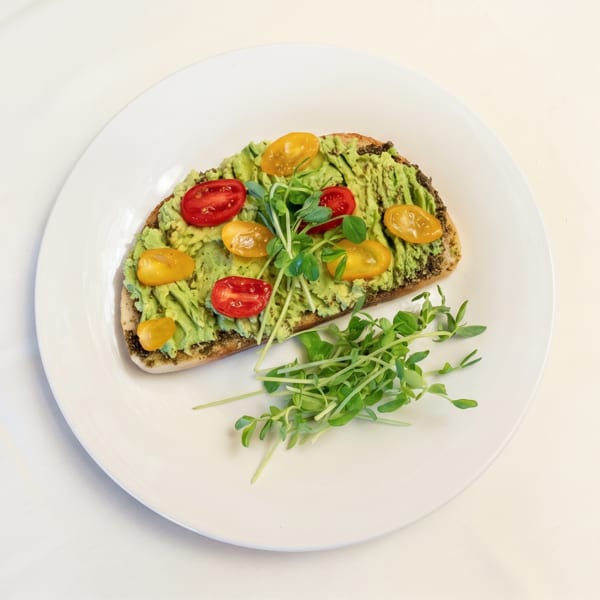 Avocado toast with red and yellow cherry tomatoes, topped with microgreens on a white plate.